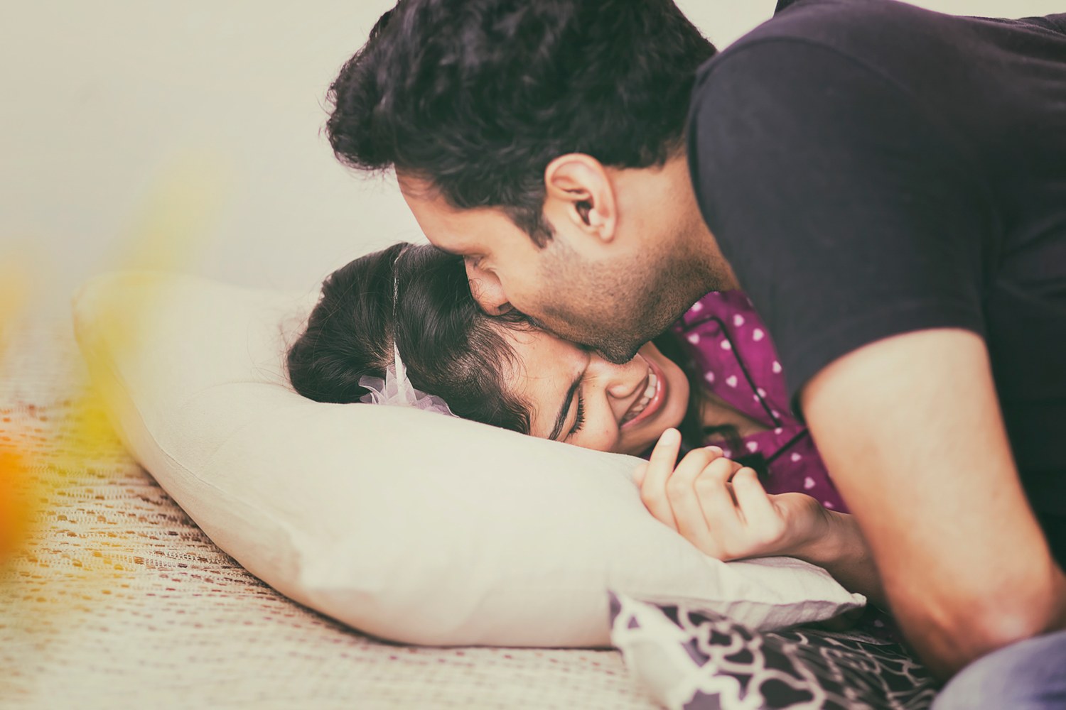 A couple lying close, one kissing the other on the head as she laughs